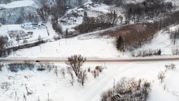 Samochód jeździ zimą po płaskiej drodze wśród wsi - widok z lotu ptaka — Wideo stockowe