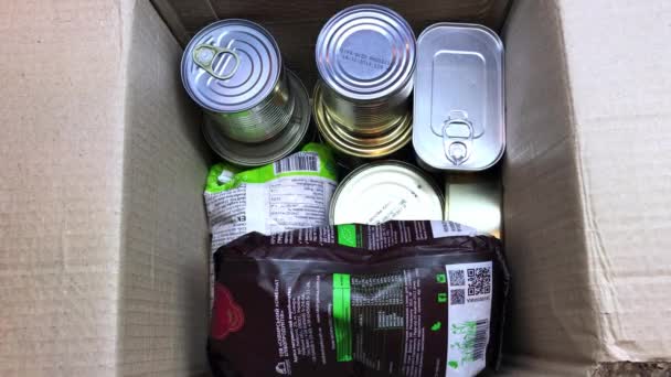 Voluntário embala alimentos enlatados e outros alimentos em caixa de papelão para ajuda — Vídeo de Stock