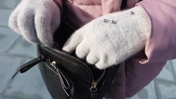 En kvinna i handskar går igenom en svart handväska och letar efter en plånbok på gatan - närbild skjuten. — Stockvideo