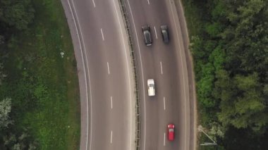 Beyaz ve siyah arabalar ve kamyonlar yeşil yapraklar arasında karayolu boyunca ilerliyorlar.