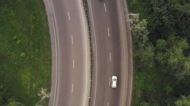 Yeşil yapraklar arasında otoyol boyunca arabalar ve kamyonlar hareket ediyor.