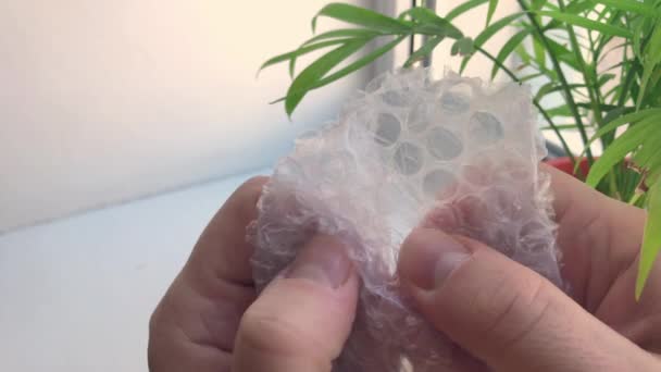 Een man drukt zijn vingers op luchtbellen in een stuk plastic bubbelfolie. — Stockvideo