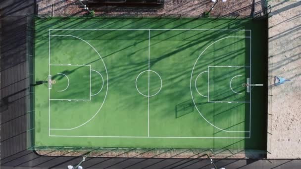 Empty green basketball court in the morning with beautiful soft shadows - top aerial view — Stock Video