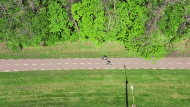 Cyclists walk along a bike path in the middle of a park near trees on a spring day — Stockvideo