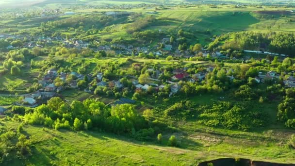 Zdjęcie lotnicze pięknych domów w wiosce wśród zielonych wzgórz w ciepły letni dzień. — Wideo stockowe