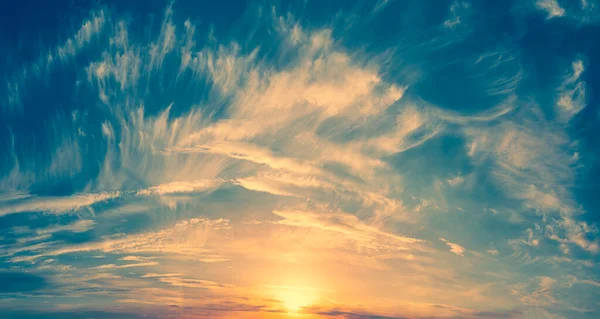 Die Sonne am Horizont malt weiße Wolken in goldener Farbe in den blauen Himmel: Sonniger Sonnenuntergang — Stockfoto