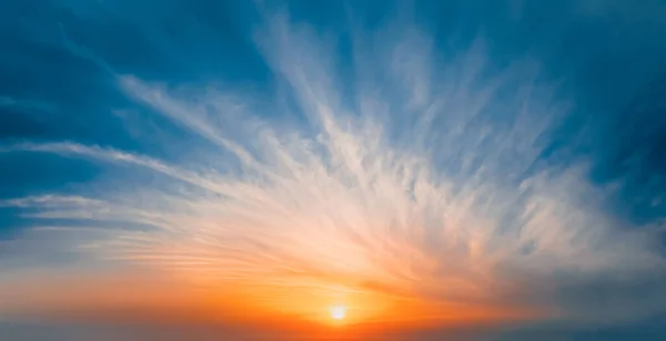 Manhã ensolarada. O sol na borda do horizonte pinta nuvens brancas no céu azul em cor dourada — Fotografia de Stock
