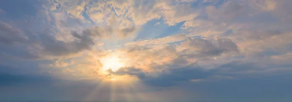 The sun in the blue sky with clouds. Rays shine through the clouds. Panoramic shot. — Stock Photo, Image