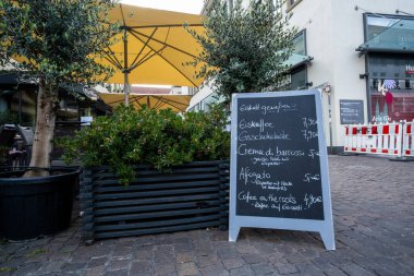 WURZBURG, GERMANY - JUNE 14, 2025 - outdoor restaurant scene with a charming chalkboard menu, surrounded by elegant olive trees, which together create a warm and inviting atmosphere for all guests