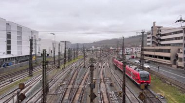 WURZBURG, GERMANY - JULY 15, 2025 - elevated view of a passenger train likely a Deutsche Bahn service navigating a busy railway station area with multiple tracks and urban buildings on a cloudy day