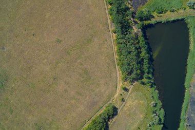 Dikey hava görüntüsü, insan yapımı karanlık bir su deposu ile açık kahverengi bir alan arasındaki keskin sınırı gösteriyor. Ağaçlarla ayrılmış. Konseptler arasında sulama, arazi kullanımı ve kuraklık yer alıyor.