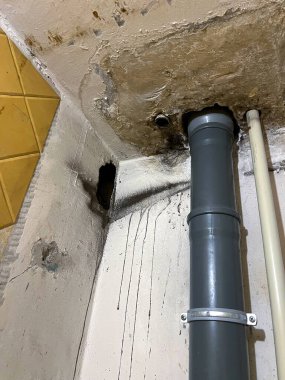 Residential interior showing severe water damage, damp patches, and mold on the ceiling and walls around a poorly sealed PVC plumbing pipe. Neglect, infrastructure failure, home maintenance problems.
