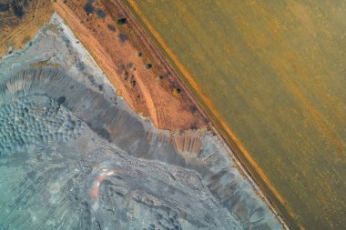Yukarıdan aşağıya doğru çekilen fotoğraf zehirli endüstriyel atık yığınıyla yeşil ekin alanı arasında keskin bir sınır olduğunu gösteriyor. Çevre kirliliği ve arazi kullanımı çatışmasının kavramsal görüntüsü.