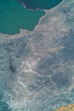 Keskin bir kirlilik sınırının dikey hava görüntüsü. Zümrüt yeşili endüstriyel su, karmaşık erozyon ve akış şekilleri gösteren geniş mavi-gri kuyruk arazisiyle çelişiyor. Kirli su deposu.
