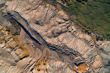 Heykeltraş edilmiş, aşınmış endüstriyel atıkların soyut hava görüntüsü. Açık gri kahverengi yeryüzü yoğun jeolojik akış şekilleri gösteriyor. Koyu yeşil doğal sınırlarla tamamen zıt..