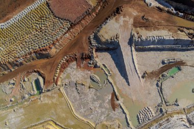 Soyut insansız hava aracı atışı bir açık çukur mayınının geometrik desenlerini yakalıyor. Kırmızı kil, beyaz toprak ve karanlık toprak arasındaki keskin zikzak köşeleri çarpıcı bir endüstriyel doku oluşturarak çıkarmayı ön plana çıkarıyor..