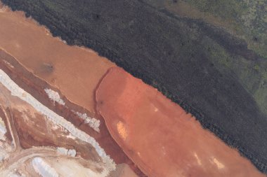 Drone, koyu toprak, kırmızı-kahverengi toprak ve beyaz jeolojik katmanlar arasındaki çarpıcı çapraz kontrastı yakalıyor. Güçlü renk blokları cesur, soyut bir endüstriyel arkaplan oluşturuyor..