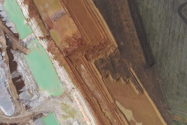 Katmanlı maden malzemeleriyle karanlık dünya arasındaki keskin çapraz sınırın insansız hava aracı atışı. Açık çukur kazılarında parlak deniz mavisi kimyasal su havuzları ciddi endüstriyel kirliliği gösteriyor.