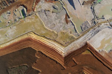 Soyut insansız hava aracı atışı bir açık çukur mayınının geometrik desenlerini yakalıyor. Kırmızı kil, beyaz toprak ve karanlık toprak arasındaki keskin zikzak köşeleri çarpıcı bir endüstriyel doku oluşturarak çıkarmayı ön plana çıkarıyor..