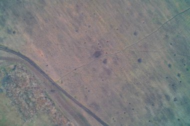 Toprak yolun yanındaki kuru ve yaralı bir araziden geçen karmaşık bir araç hattının insansız hava aracı görüntüsü. Savaş alanı lojistik rotaları ve ince kabuklu kraterler. Sert tarım arazisi dokusu.