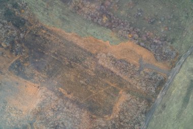 Yanmış yamalar ve toprak bir yoldan gelen araç izleri olan dokulu bir alanın hava aracı görüntüsü. Ağaç çizgisi ve pürüzlü yüzeyi olan sonbahar kırsal arazisi. Potansiyel çatışma bölgesinde lojistik model ve çevresel hasar.