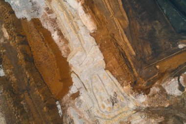 Açık maden ya da endüstriyel bozulma uçlarının canlı, soyut hava görüntüsü koyu siyah ve kırmızımsı kahverengiyle beyaz kil arasındaki yoğun renk kontrastında ham jeolojik katman gösteriyor..