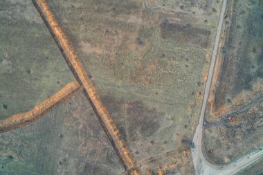 Karayolu kavşağında turuncu kil bulunan geniş toprak siperlerinin yukarıdan aşağıya doğru görüntüsü. Sahnede, harap olmuş askeri araçların paslanmış enkazı yer alıyor. Bu da savaş savunmasının şiddetini gösteriyor.