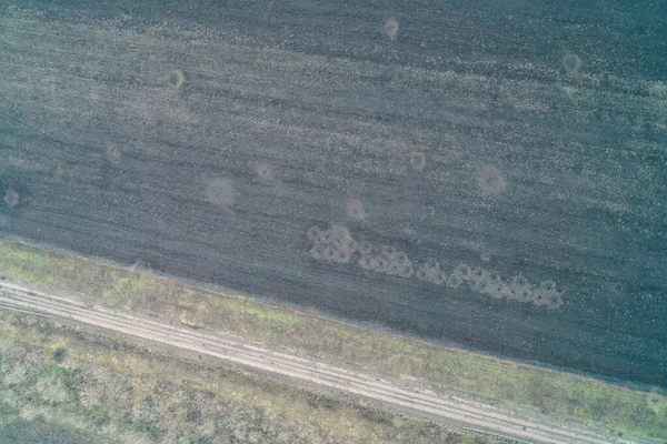 Kümelenmiş çarpışma kraterlerinin ve toprak yol ve ağaç hattının bitişiğindeki bombardıman izlerinin bulunduğu çorak bir tarım alanı. Bu ıssız arazi, askeri faaliyetlerin yakın çevresini ve tarım arazileri üzerindeki yıkıcı etkisini gözler önüne seriyor.