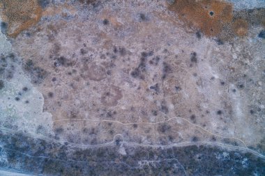 Buz kaplı bir alanın dolambaçlı yollarla çaprazlanmış dokulu bir üst görüntüsü. Soğuk kış manzarası, doğanın sessiz güzelliğini yansıtan kuru çalıları ve donmuş zemini kapsıyor..