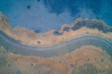 Tehlikeli sanayi bölgesinde virajlı bir köy yolu. Mavi zehirli atık ve kuru turuncu alan arasındaki yüksek çözünürlüklü zıtlık, fotokopi alanı ile yatay üst görünüm drone görüntüsü.