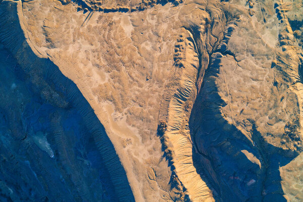 Stunning aerial top view of industrial clay dumps featuring eroded ridges. The high contrast between sunlit orange earth and deep blue shadows creates a surreal abstract pattern resembling an alien landscape or Mars terrain texture.