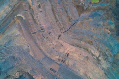 Derin çatlaklar ve teraslı kil katmanların yer aldığı çarpıcı bir sanayi manzarası. Kırmızımsı toprak ve mavi mineral yataklarının karışımı toprak erozyonu ve çevresel etkiyi temsil eden engebeli bir soyut doku yaratır..