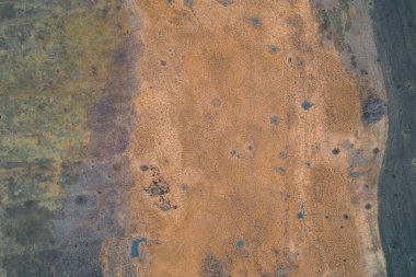 Yeşil ottan kuru turuncu sazlıklara ve karanlık toprağa geçiş yapan bataklık arazisinin yukarıdan aşağıya havadan görünüşü. Doku yapısı, sonbahar mevsimini, kırsal yabanı ve kuruyan toprağı sembolize eden doğal bir kamuflaj modeline benziyor..