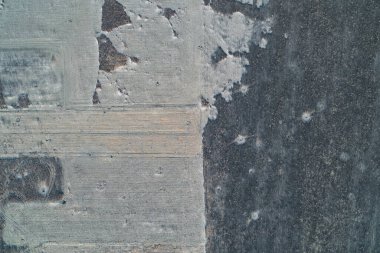 Toprak dokularının zıt olduğu bölünmüş tarım arazilerinin geometrik hava görüntüsü. Minimalist kompozisyon, kara toprağı buzlu yamalar ve kuru sakallarla harmanlayarak tasarım kavramları için doğal bir soyut zemin oluşturur..