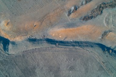 Olaysız arazi, gri ve turuncu kil manzarasını aşan derin bir çatlağı ortaya çıkarıyor. Dokulu toprak yüzeyinde doğal erozyon desenleri ve kazı izleri, jeolojiyi, arazi bozulmasını ve inşaat kavramlarını gösteriyor..