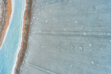 Buz gibi kıvrımlı nehir, dağınık kar parçalarıyla donuk bir tarla ile çevrili. Hava aracı fotoğrafçılığı. Bu kış arazisi soğuk mevsimsel dokulara sahip çarpıcı bir soyut arkaplan sağlar..