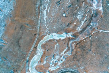 Buzla kaplı, dokulu, kahverengi kış manzarası boyunca akan buz gibi bir akarsu. İHA atışı. Karmaşık doğal desenler mevsimsel tasarım için benzersiz bir soyut çevre arka planı oluşturur..