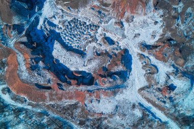 Kil ocağı kazıları, beyaz kış karıyla zıt düşen koyu kırmızımsı turuncu toprağı ortaya çıkardı. Endüstriyel madencilik izleri, soğuk bir arazide insan aktivitesinin ve doğanın kesişimini gösteren ham, soyut bir jeolojik desen oluşturur..