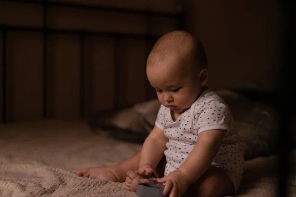 Infant boy sits in the bed and plays with toy in cozy room. High quality photo.