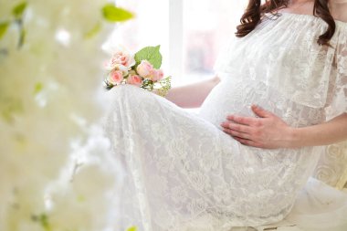 Güzel, genç, hamile bir kadın elleriyle karnını okşuyor..