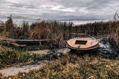 Nehir kıyısında. Uzun, kuru ot. Eski tekneler ve lastikler.