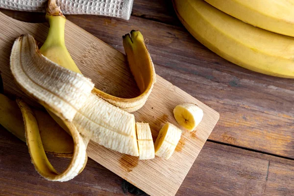 Banana slices on a wooden board and banana fruit in the background