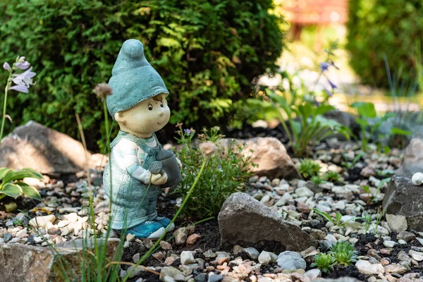 Bahçede bir cüce. Dekoratif heykeller. Peyzaj dekoru. Bahçede bir taş. Yeşil bahçe. Bir erkek heykeli.