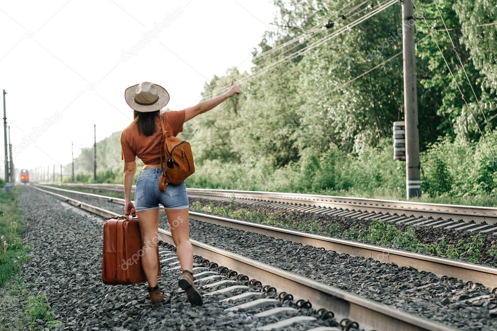 landscape with railway leading lines. A girl with a suitcase and a backpack. The traveler.