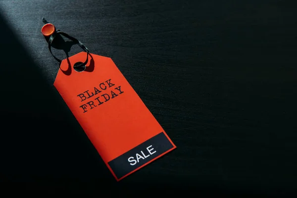 Concept image of label with inscription on dark wooden background, combination of light and shadow. Red tag Black Friday, close-up, copy space.