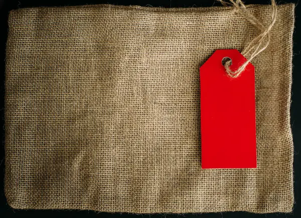 Concept image of an empty label and canvas bag on dark background, copy space. Red tag on a string, close-up.