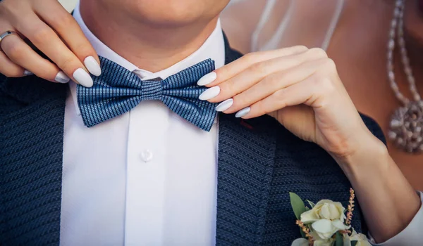 Bow tie on the groom's suit. Bride's hands touch the tie of her betrothed, close up. Theme of the wedding, newlyweds, love.