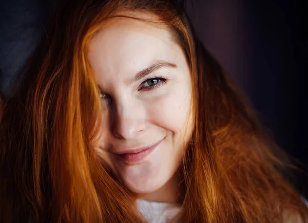 Portrait of beautiful young woman with thick, tousled red hair, close-up. Gray-eyed beauty looking at camera and smiling. Advertising of skin or hair care.