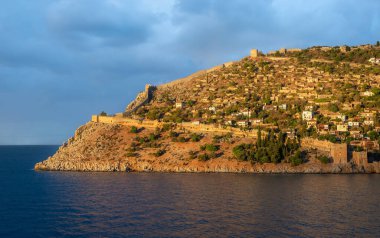 Altın gün batımı ışığı Alanya Şatosu 'nu ve Alanya Türkiye' deki Akdeniz 'in üzerindeki antik kale duvarlarını aydınlatarak tarihi mimari ve manzaralı kıyı güzelliğini gözler önüne seriyor.