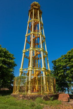 Puerto Plata, Dominik Cumhuriyeti 'ndeki tarihi El Faro deniz feneri, güneşli bir günde, mavi gökyüzü, yeşil ağaçlar ve Karayip mirasını sembolize eden ikonik demir yapısı ile